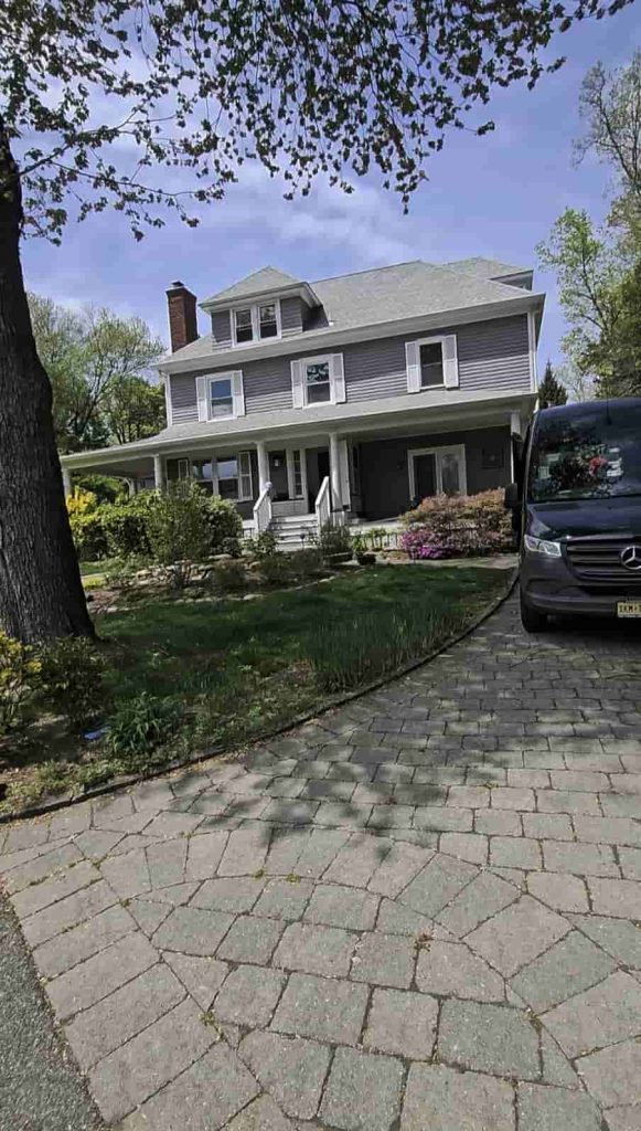 A black Mercedes Sprinter cleaning service van parked at a grey colonial home with white porch