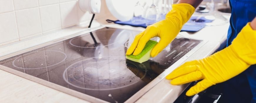 Person wearing yellow gloves cleaning stovetop as part of a move in cleaning checklist for the kitchen.