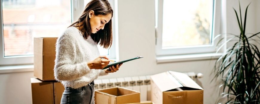 Woman checking tasks on clipboard surrounded by boxes during a deep clean before moving in.