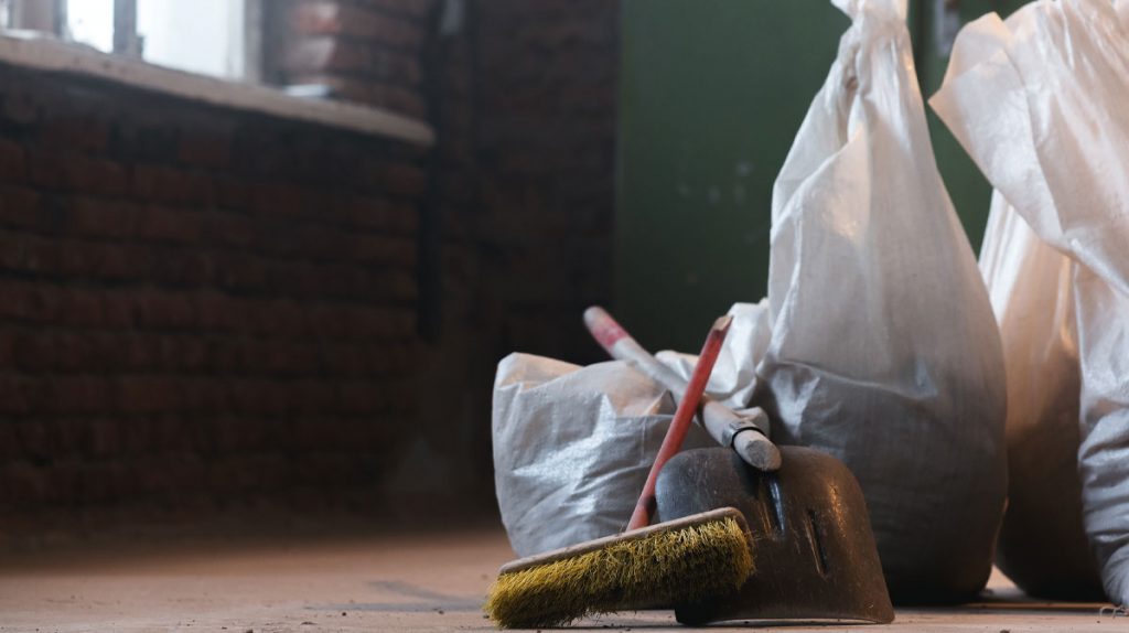 Construction dust cleanup with debris bags, broom, and tools inside a home renovation project.