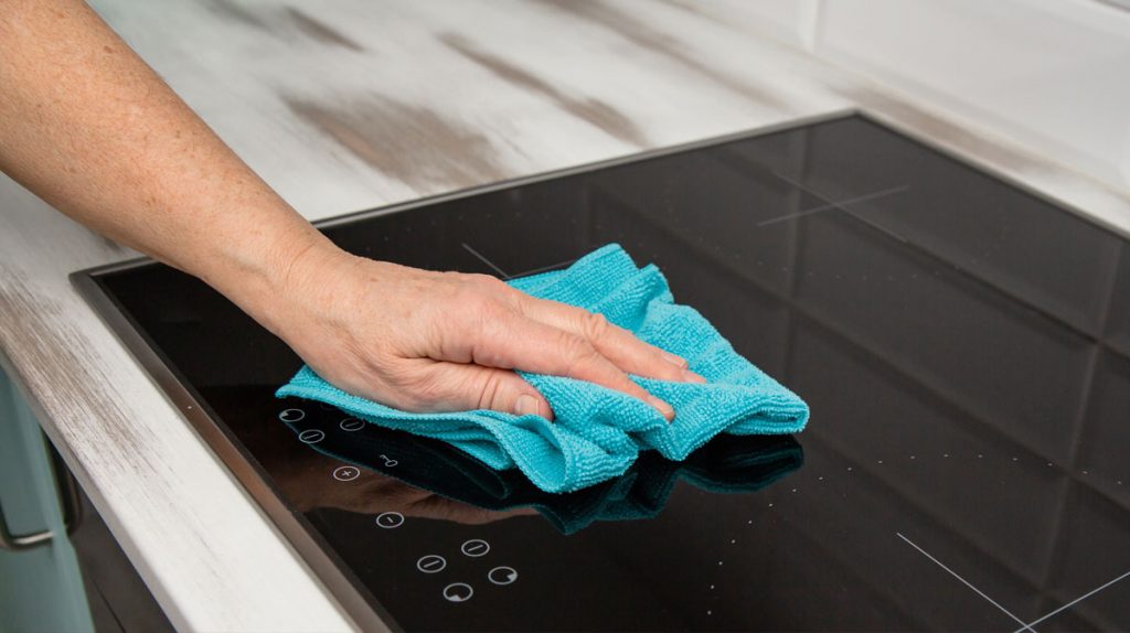 Kitchen surface cleaning during post-renovation cleanup using a microfiber cloth to remove construction dust and residue.