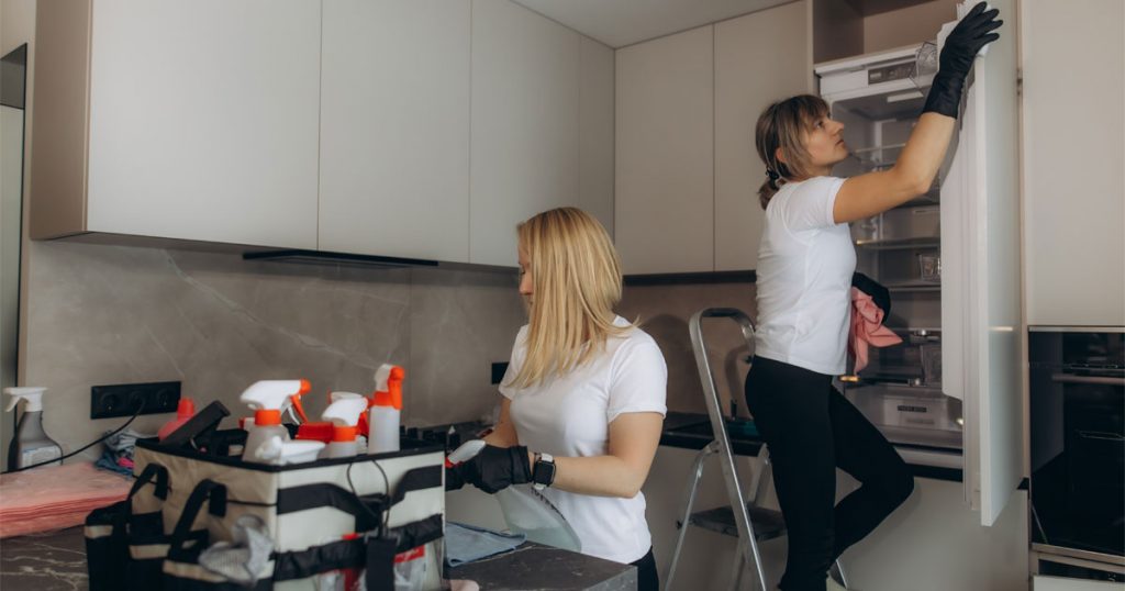 Professional cleaners performing a move-out deep cleaning in a modern kitchen, including appliance and cabinet cleaning