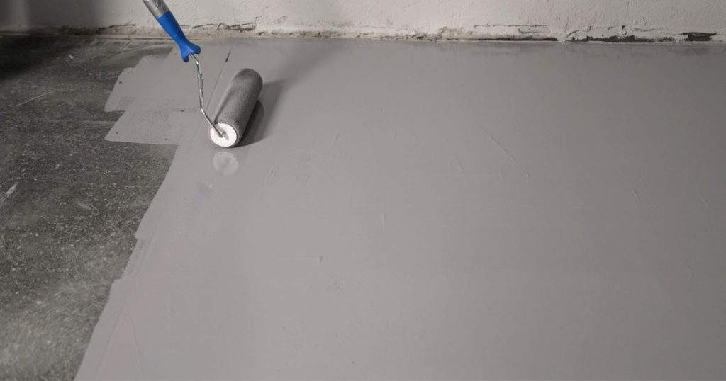Contractor applying gray epoxy floor coating to a concrete basement floor during professional epoxy flooring installation.