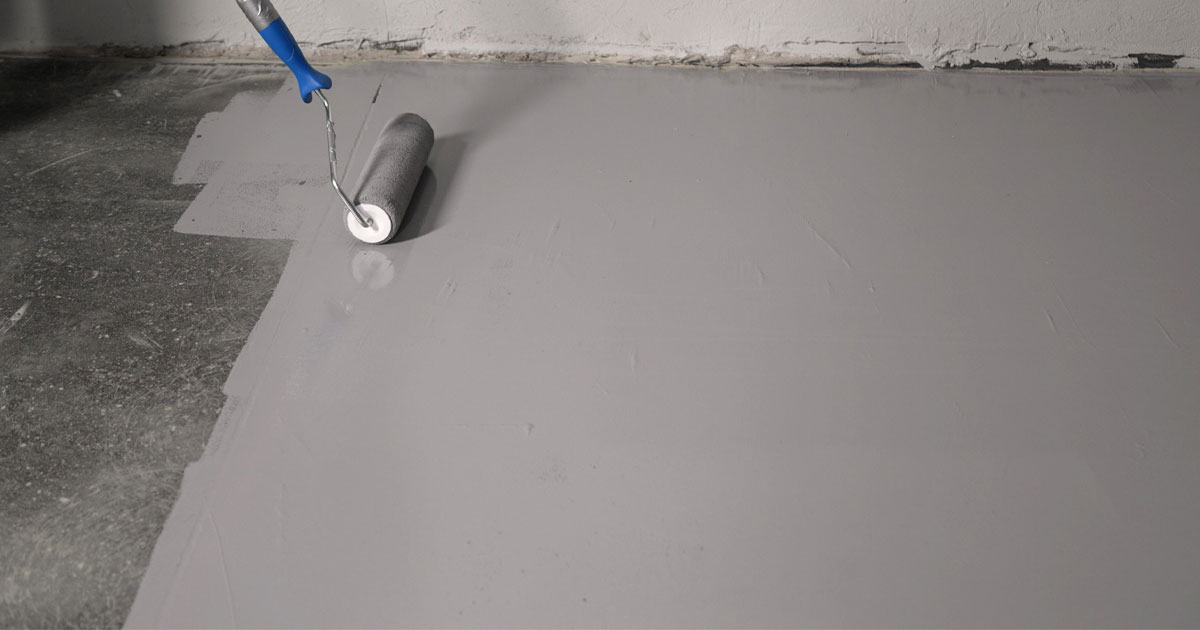 Contractor applying gray epoxy floor coating to a concrete basement floor during professional epoxy flooring installation.