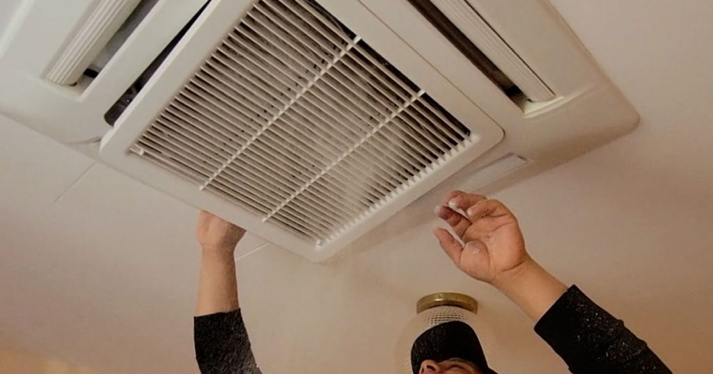 Technician removing construction dust from ceiling HVAC vent during post-construction cleaning